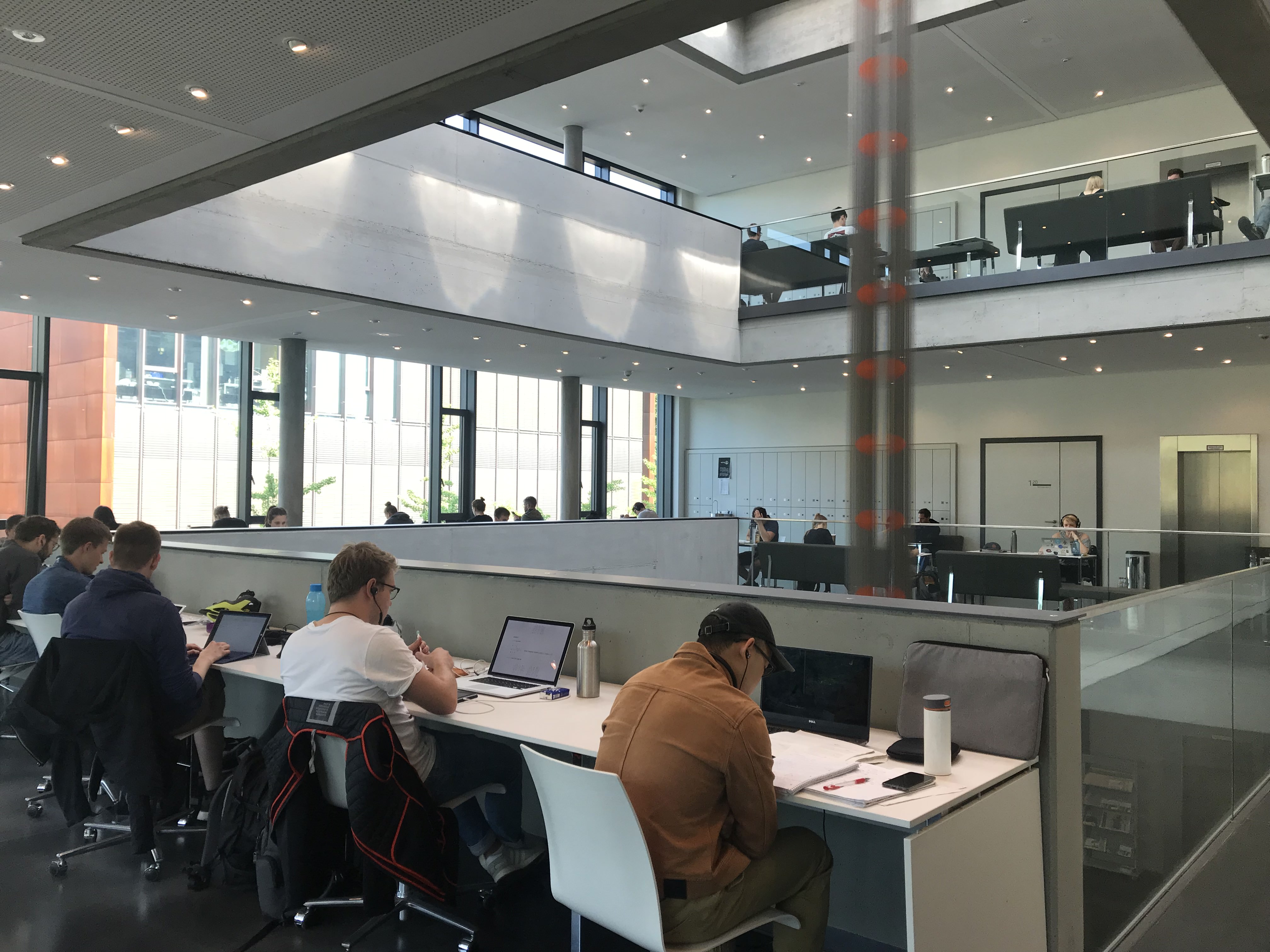KIT Studierende sitzen an Einzeltischen im lichtdurchfluteten Lernzentrum am Fasanenschlösschen des Karlsruher Instituts für Technologie (KIT). Die moderne Architektur mit großen Fensterfronten und offenen Galerieebenen schafft eine ruhige Arbeitsatmosphäre.